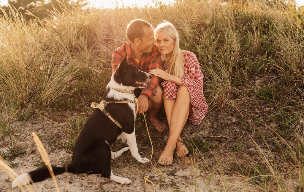 Man och kvinna på stranden i sanden med sin hund i solnedgången. Fotograferat av Satu Knape, fotograf i Linköping