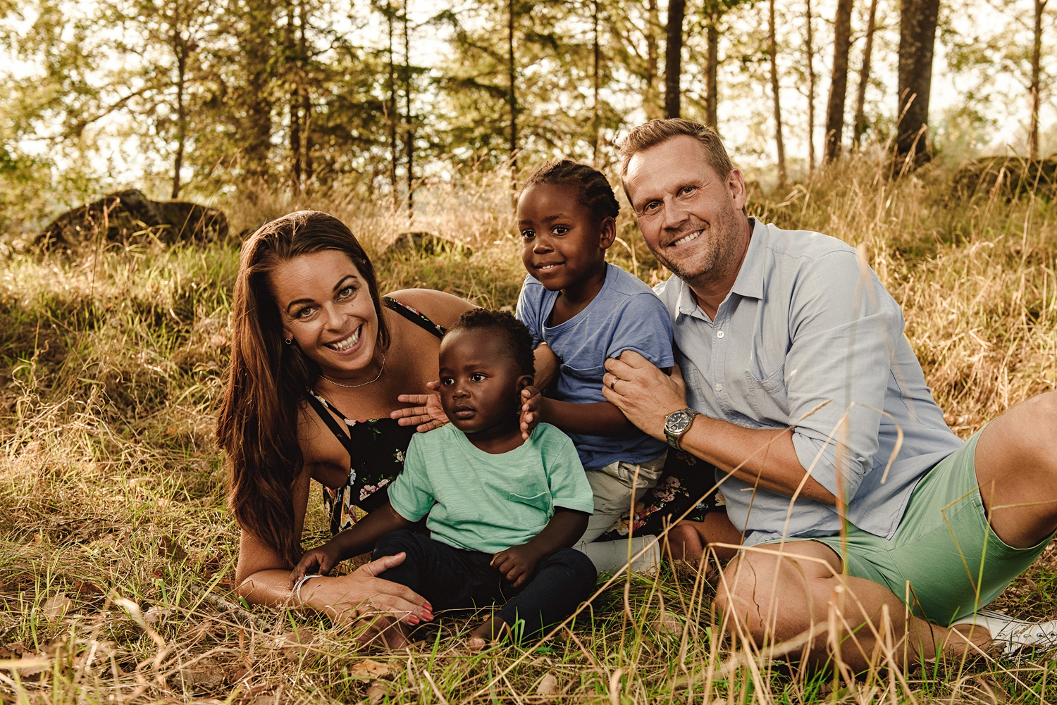 Familjefotografering utomhus i Norrköping med familj som sitter på marken. Mamma Pappa och två barn i fin skogsmiljö.